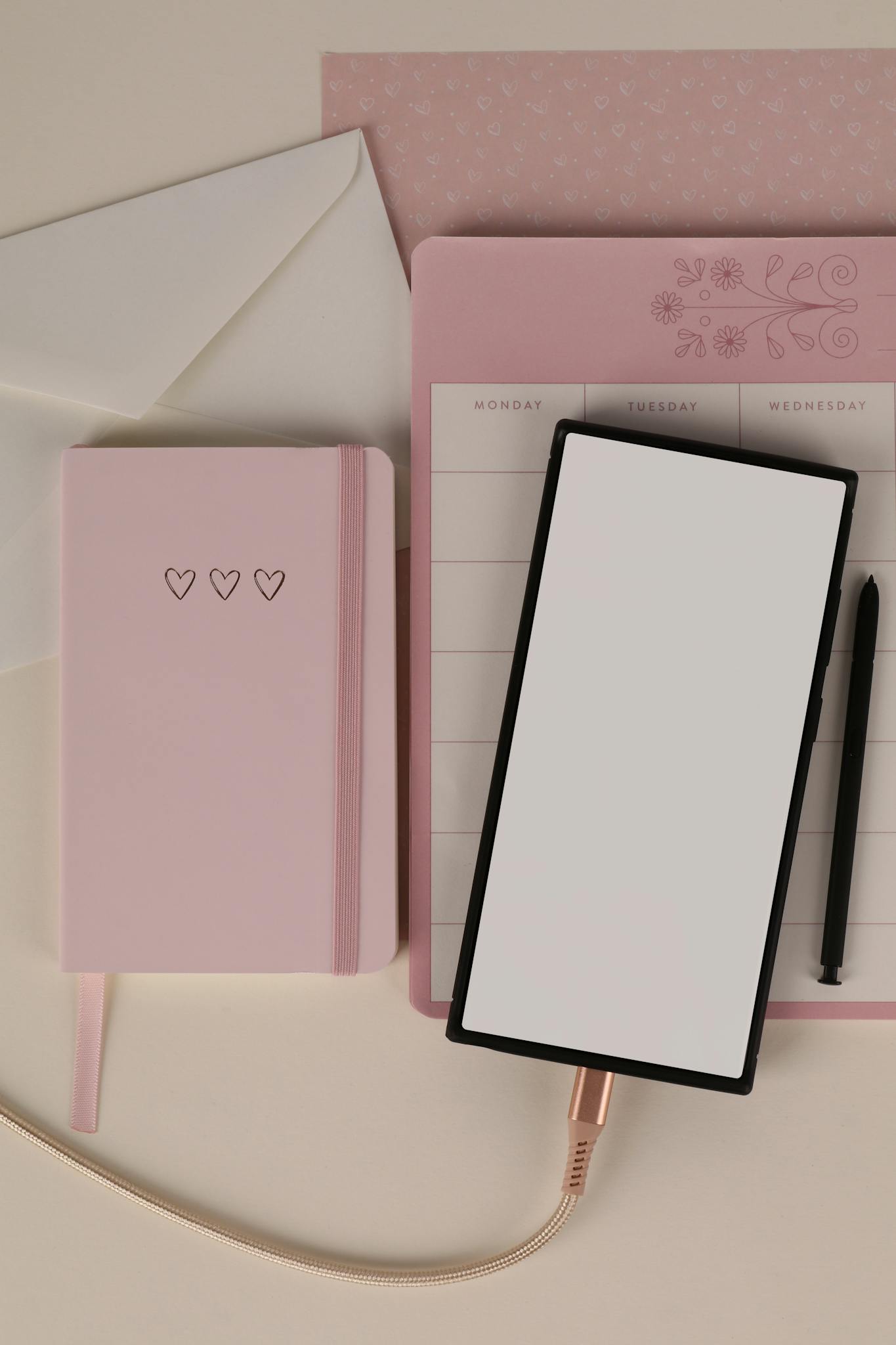 A flat lay featuring pink stationery, a blank screen tablet, and envelopes for an aesthetic workspace.