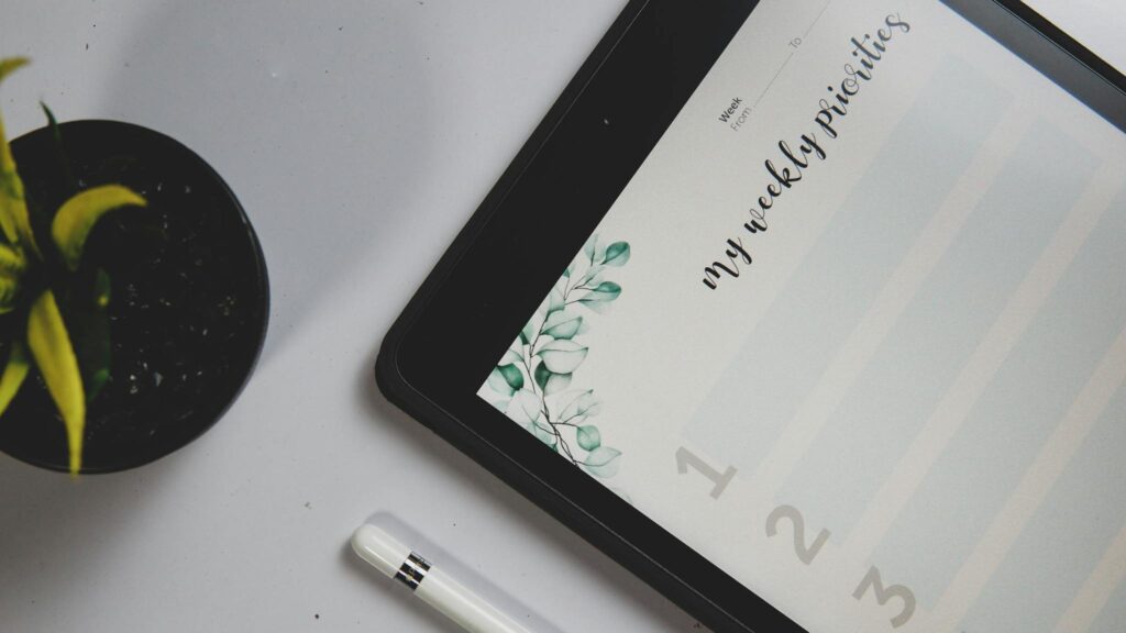Never Run Out of Ideas: Top Tips for Generating Fresh Blog Topics Close-up of a tablet displaying a weekly planner with a stylus and a potted plant on a desk.